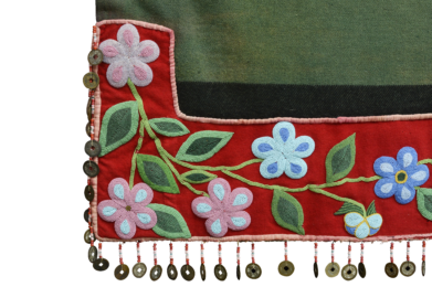 The corner of a green blanket with red trim embroidered with beads and a fringe edge with coins.