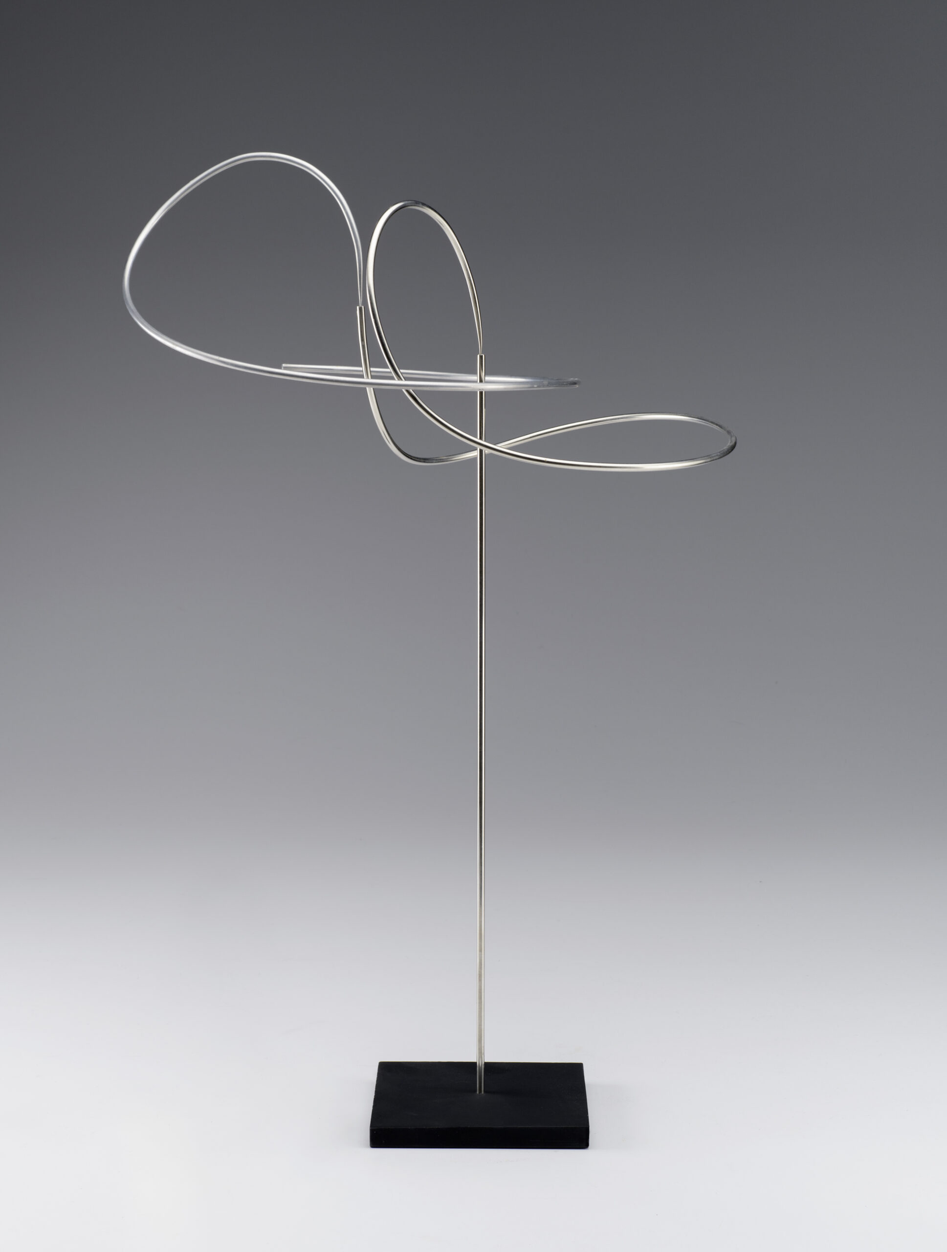 A silver sculpture of an abstract, linear shape affixed to black base. 