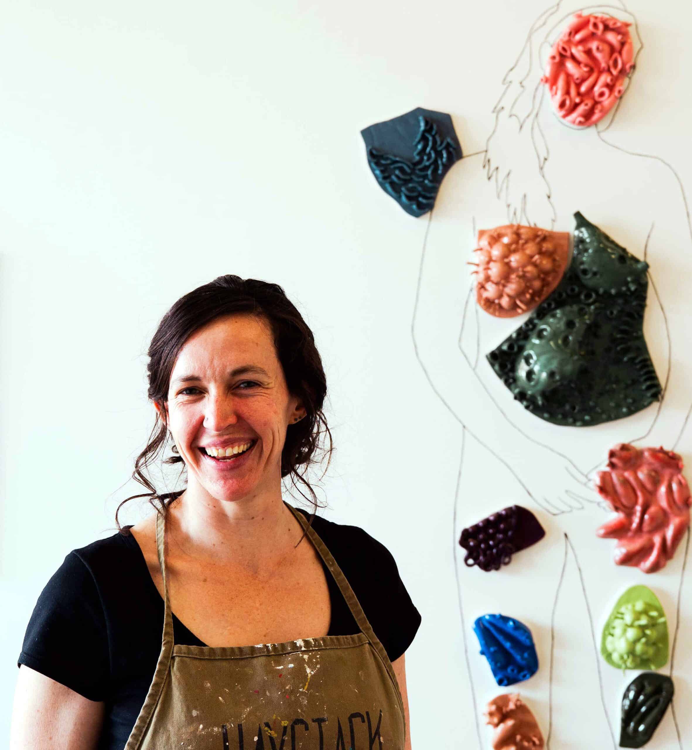 A smiling woman poses next to her ceramic installation featuring anatomical parts.
