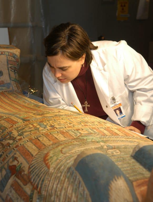 A woman in a lab coat examines images on a coffin.