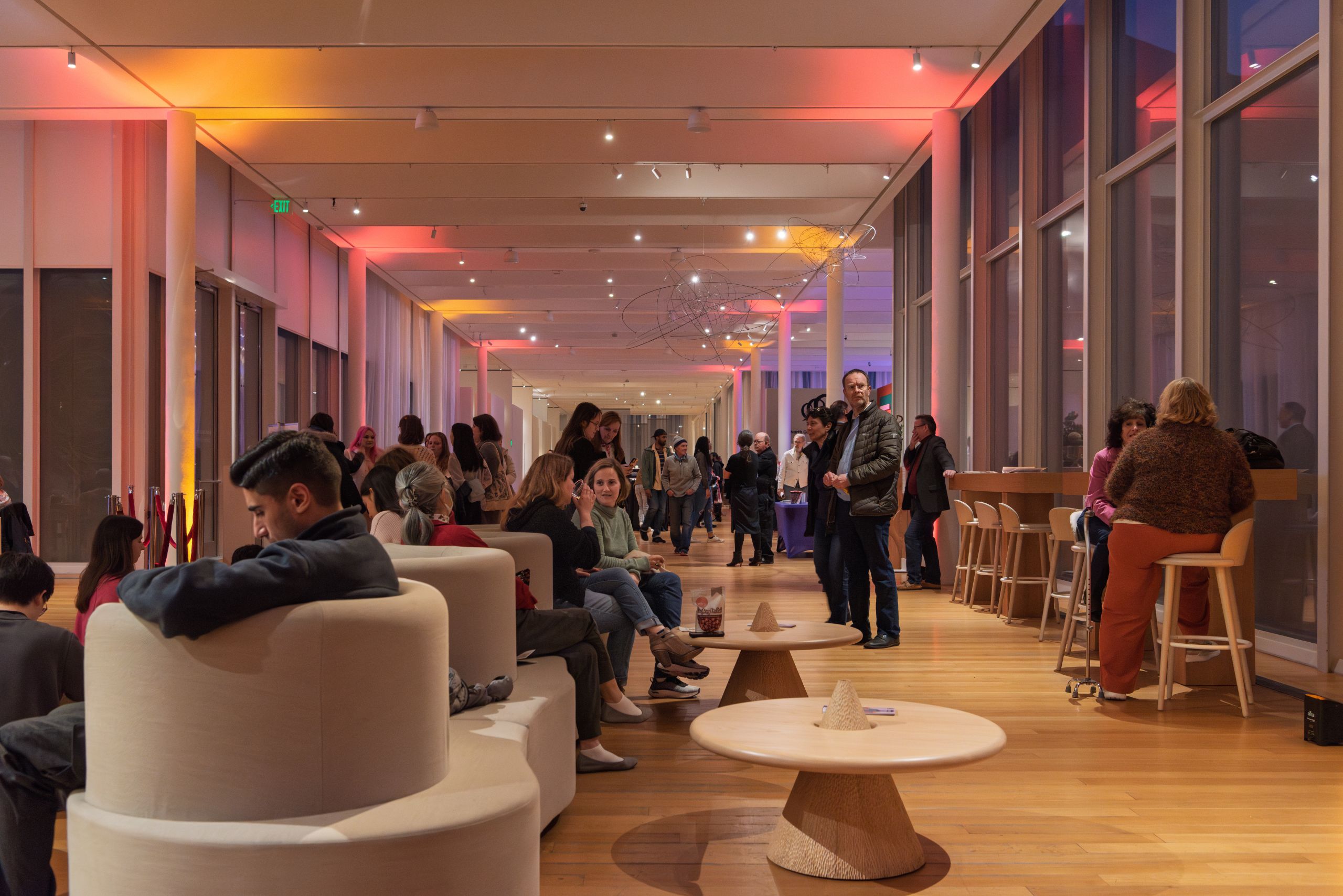 A crowd of people mingle and relax in a colorfully lit atrium.