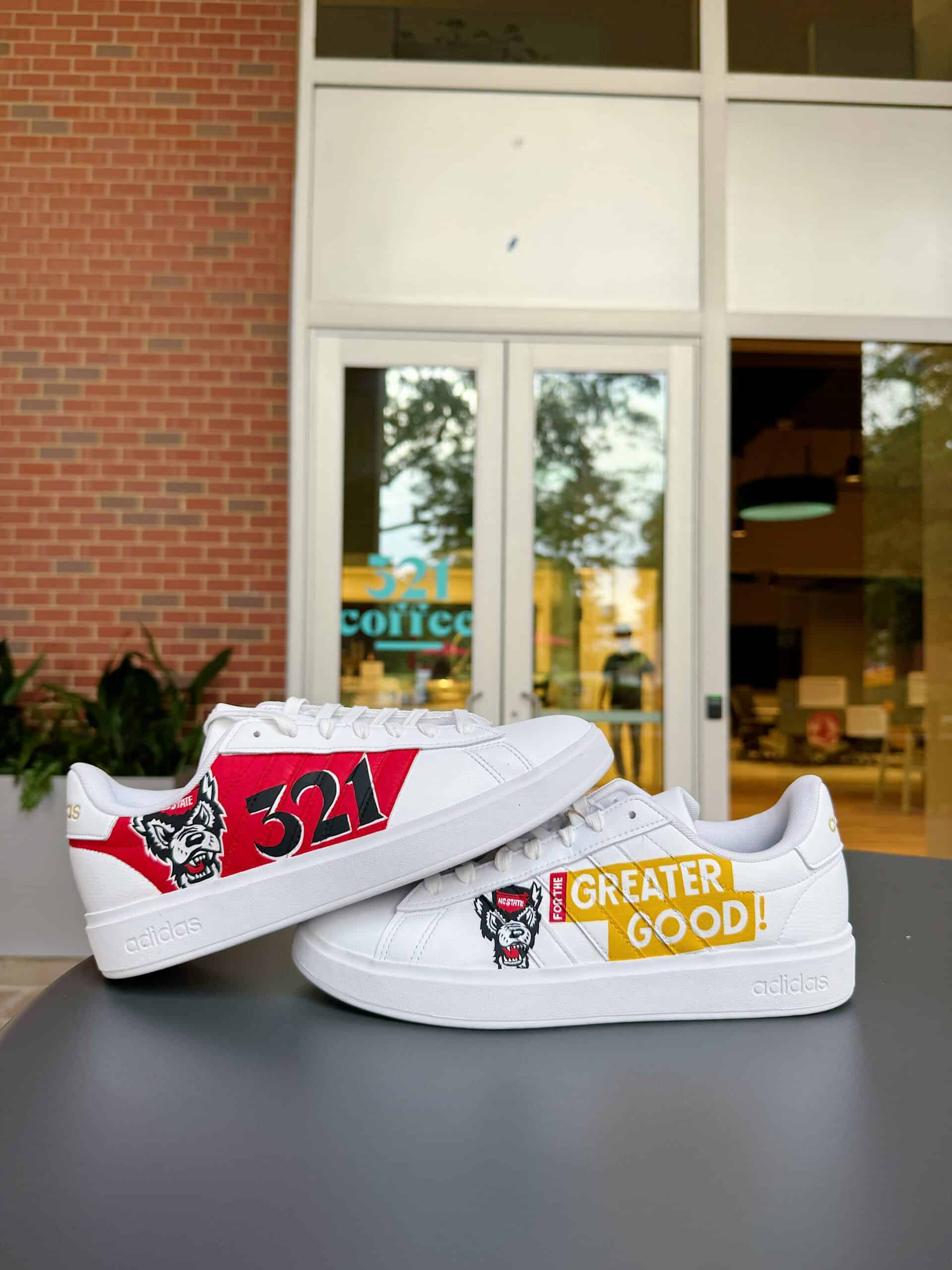 Two white sneakers with hand-painted designs placed on top of a table in front of a coffee shop.