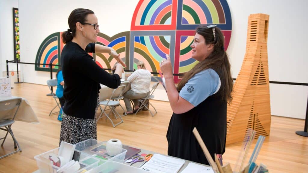 Two people face each other in an art gallery with large abstract works behind them.