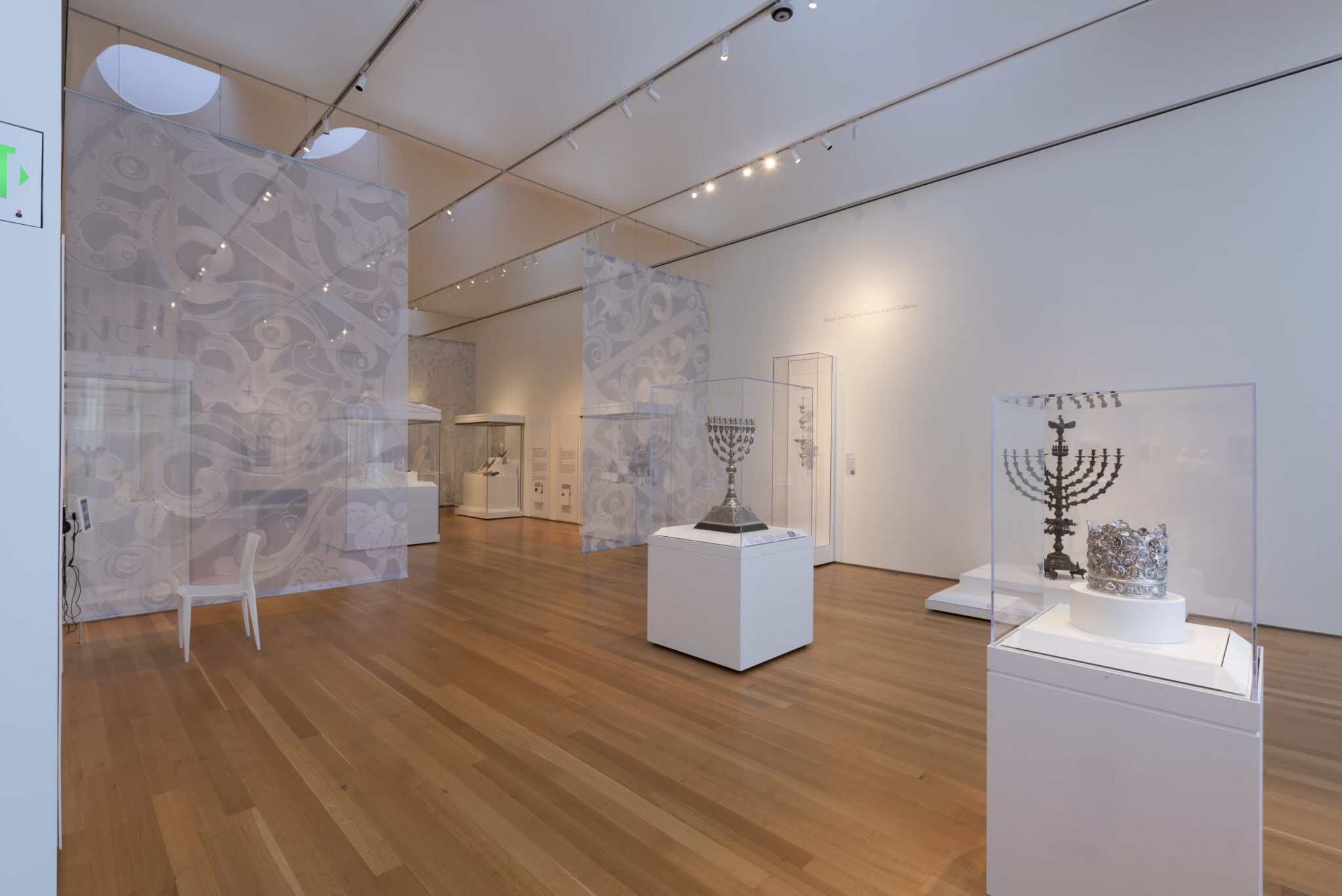 An art gallery populated with pedestals and glass cases displaying Judaica. 