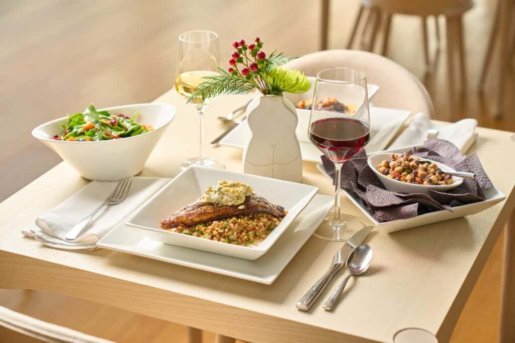 Several dishes of prepared food and filled wine glasses sit atop a set table.
