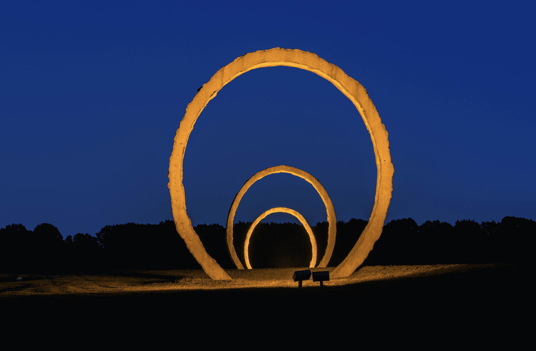 A large installation of three nested rings illuminated in a landscape at night.