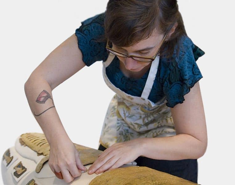 A person wearing an apron leans over and touches an ancient sarcophagus.
