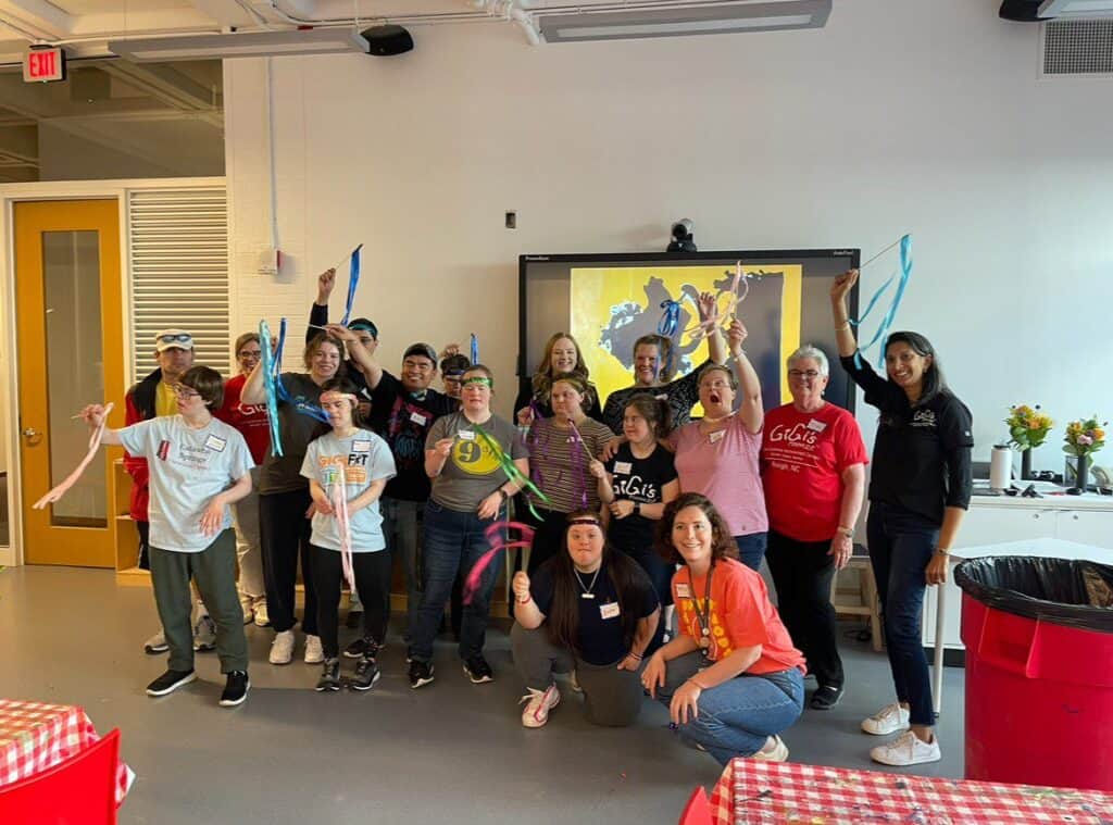 A group of people pose in front of a smart screen holding sticks with ribbons.