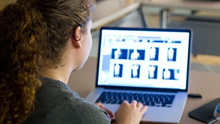 An over-the-shoulder view of a teen looking at their laptop. The screen displays a grid of indistinct images.
