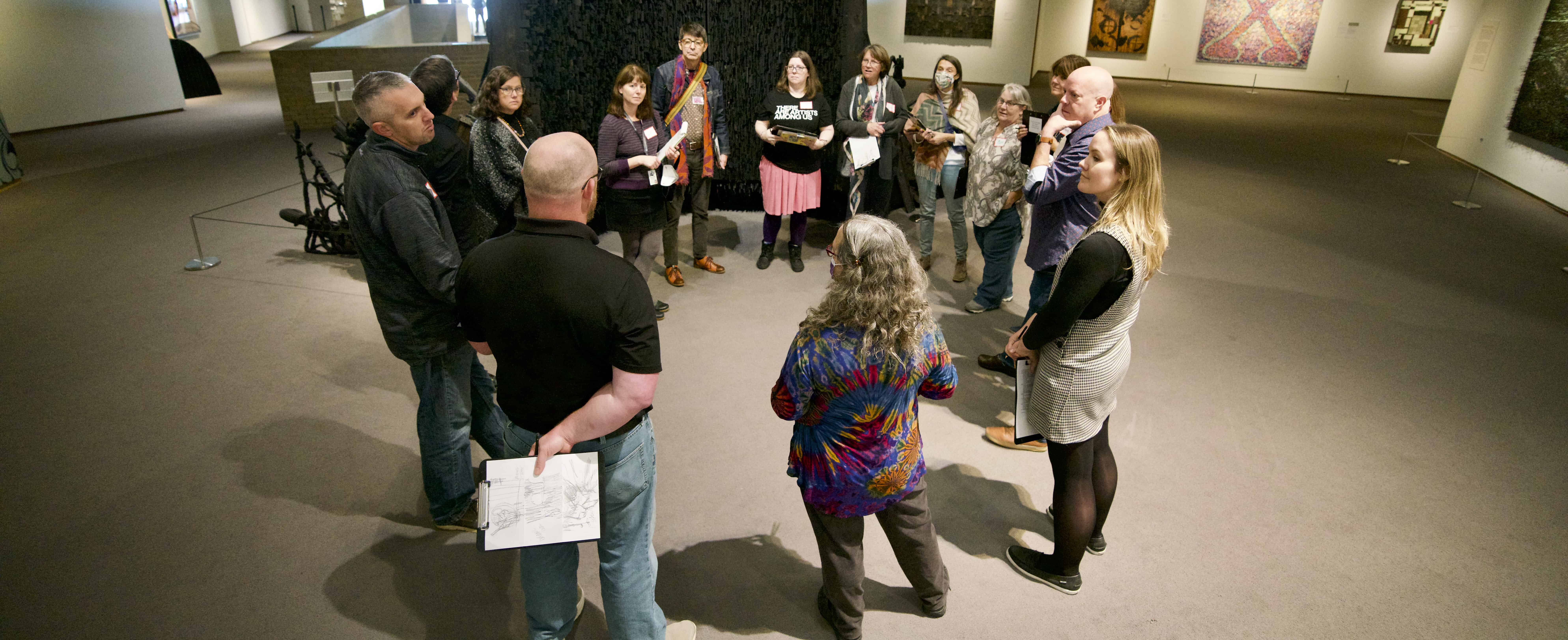 A group of people wearing name tags stand in a circle in an art gallery.