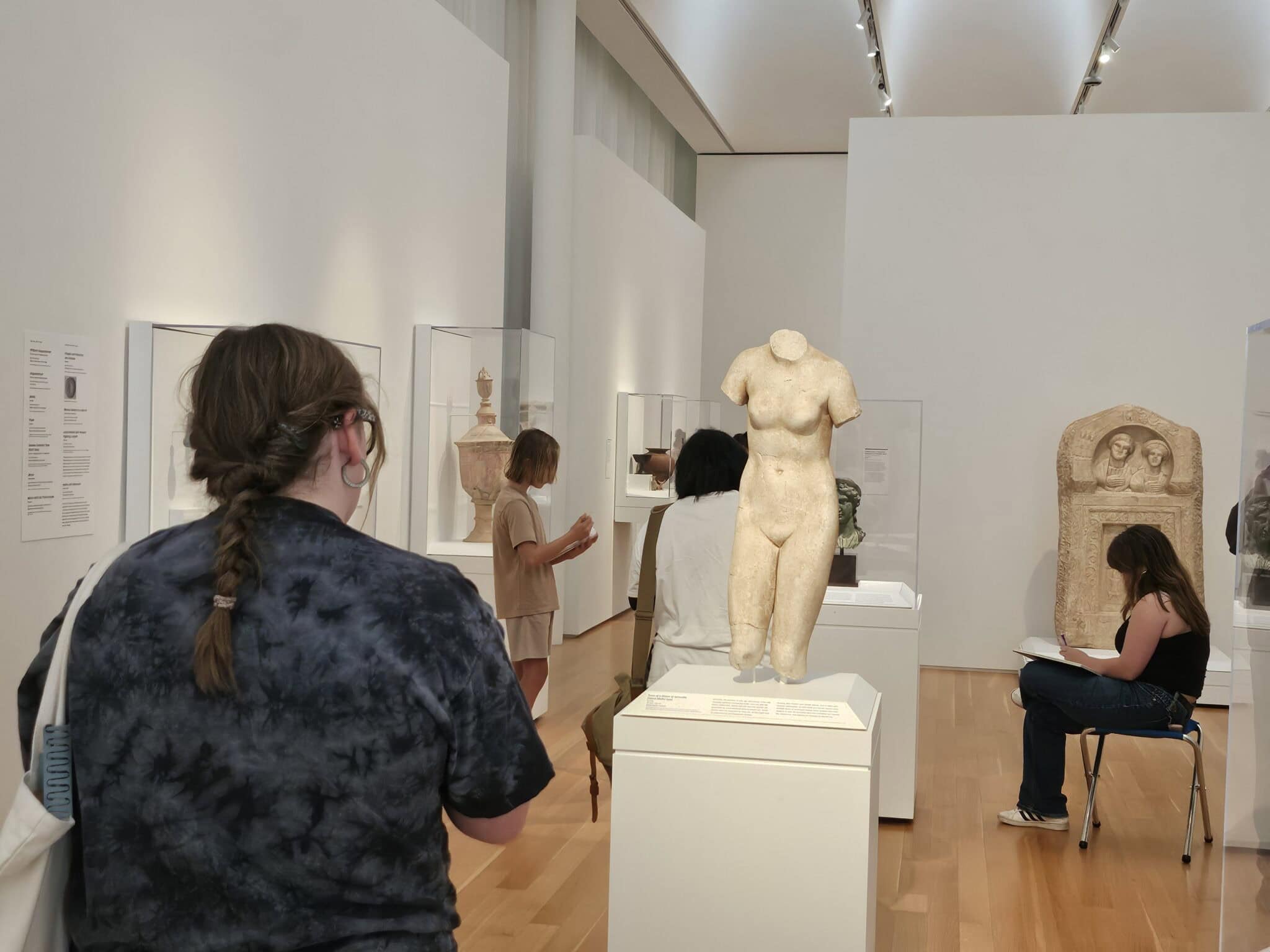 A group of teens sketching an sculpture.