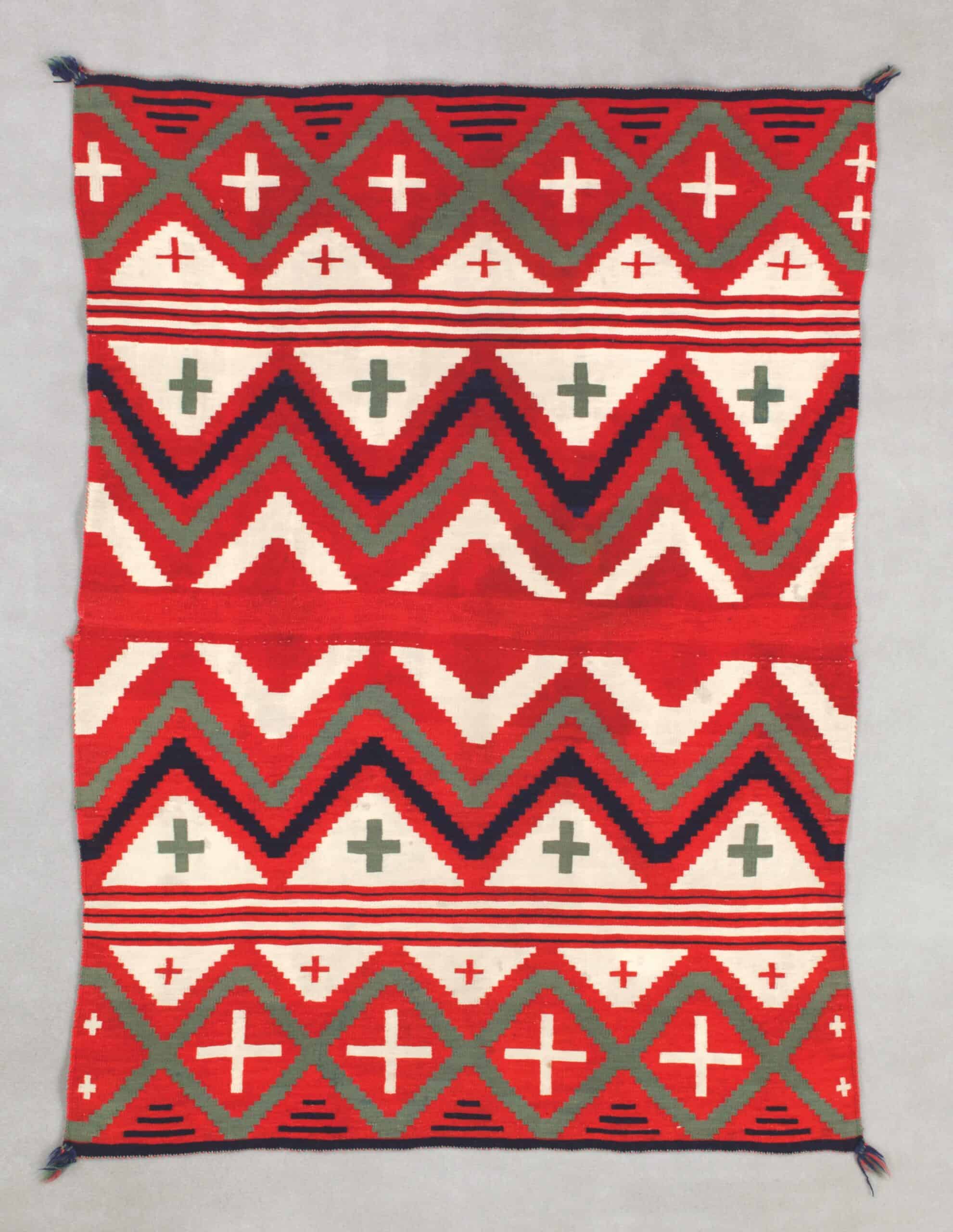 A rectangular blanket with a geometric pattern containing orange, white, and black zigzags and crosses.