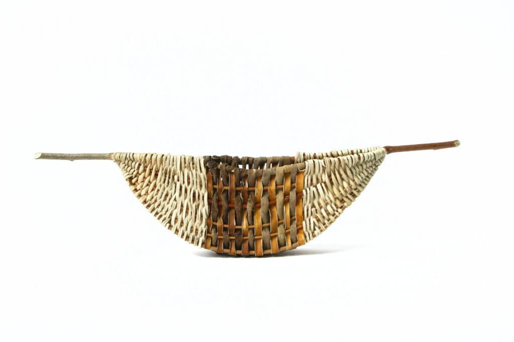 Woven basket in the form of a boat with a wide, dark brown stripe in the center and sticks protruding from each end.