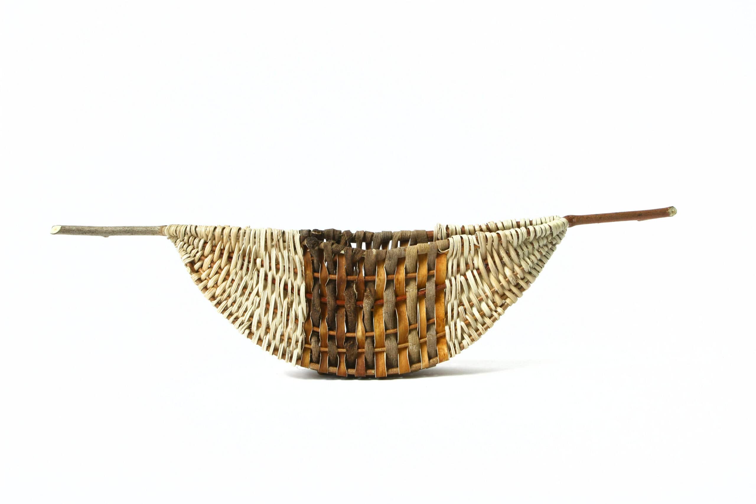 Woven basket in the form of a boat with a wide, dark brown stripe in the center and sticks protruding from each end.