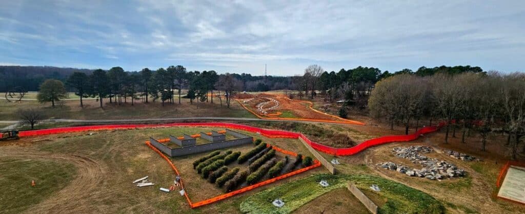 Aerial view of a landscape under construction. Orange fencing snakes throughout the grounds and building materials lie about.