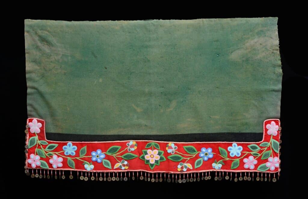 A green blanket with red trim embroidered with beads and a fringe edge with coins.