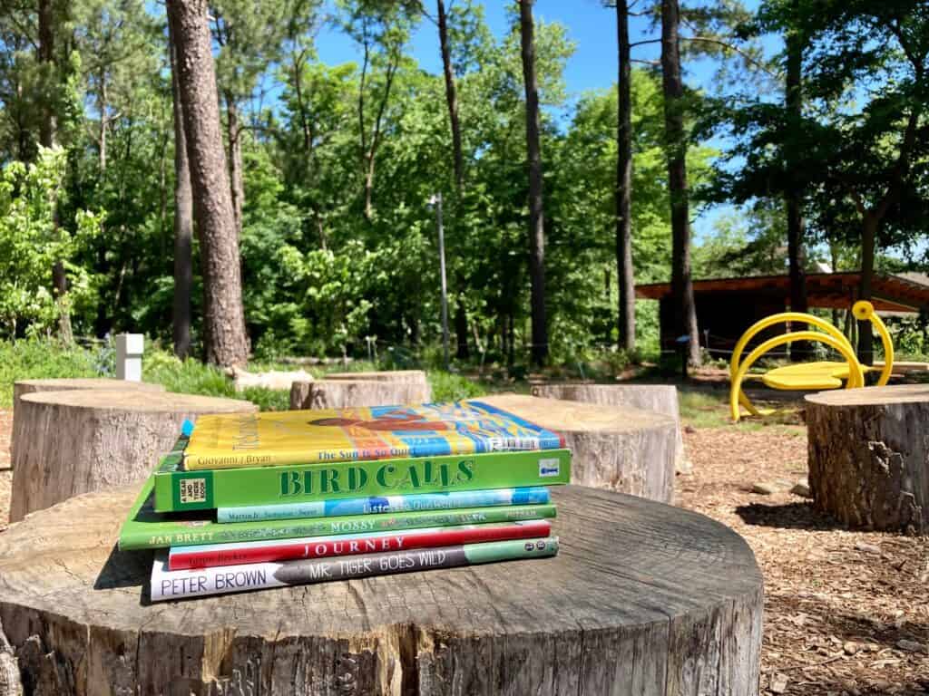 Kids’ books about nature sit on a stump in a wooded setting.