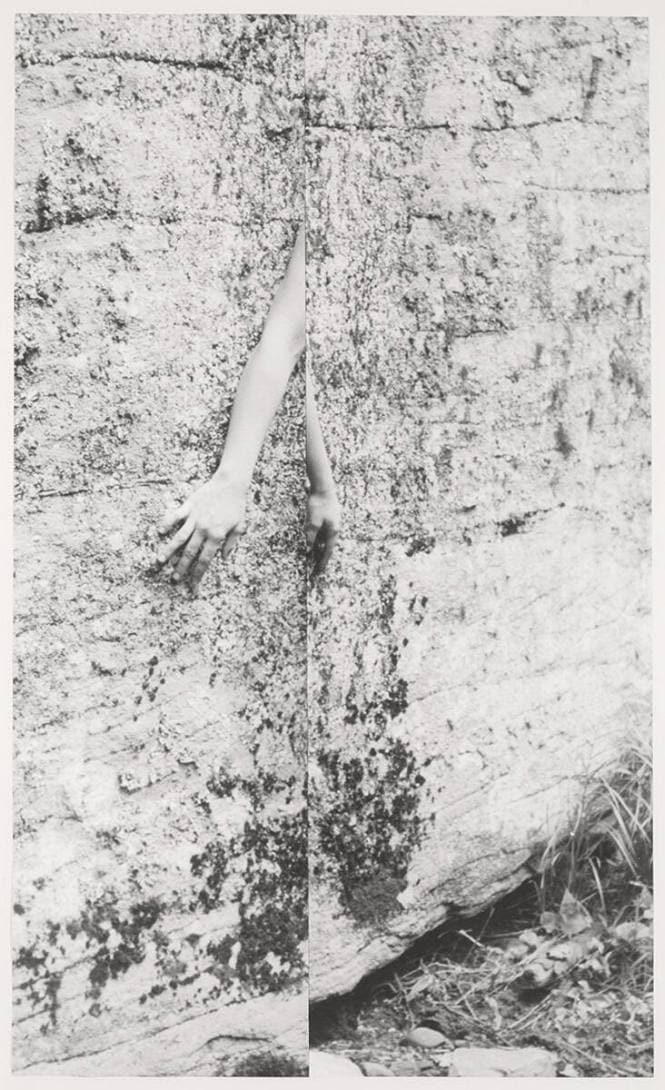Black-and-white photo of a stone wall cropped down the center in such a way that only two hands from a human body are visible.