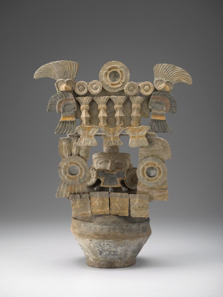 Ceramic incense burner with stacked architecture, circular motifs, and central masklike face. A bird figure with wavy feathers perches atop each side.