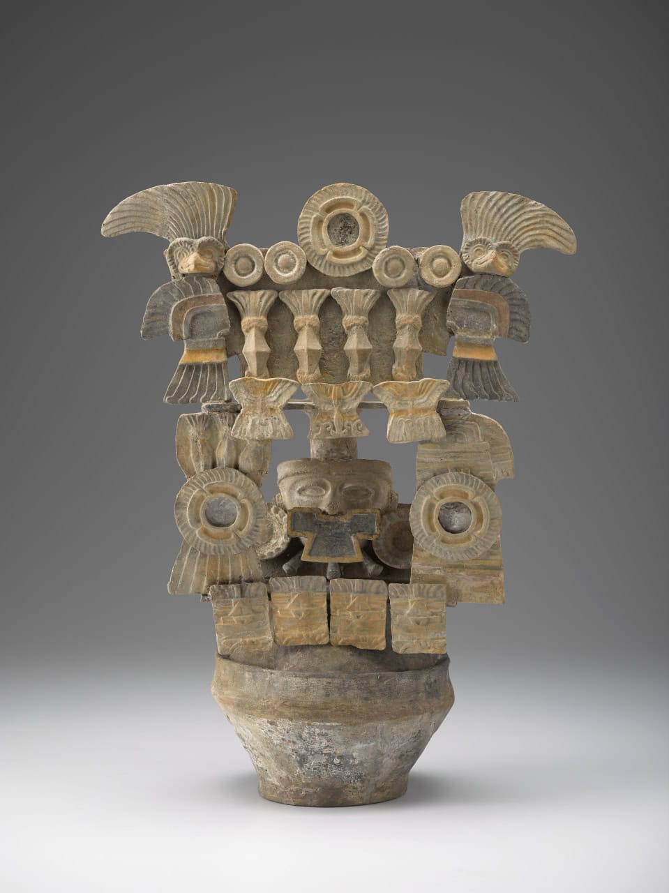 Ceramic incense burner with stacked architecture, circular motifs, and central masklike face. A bird figure with wavy feathers perches atop each side.