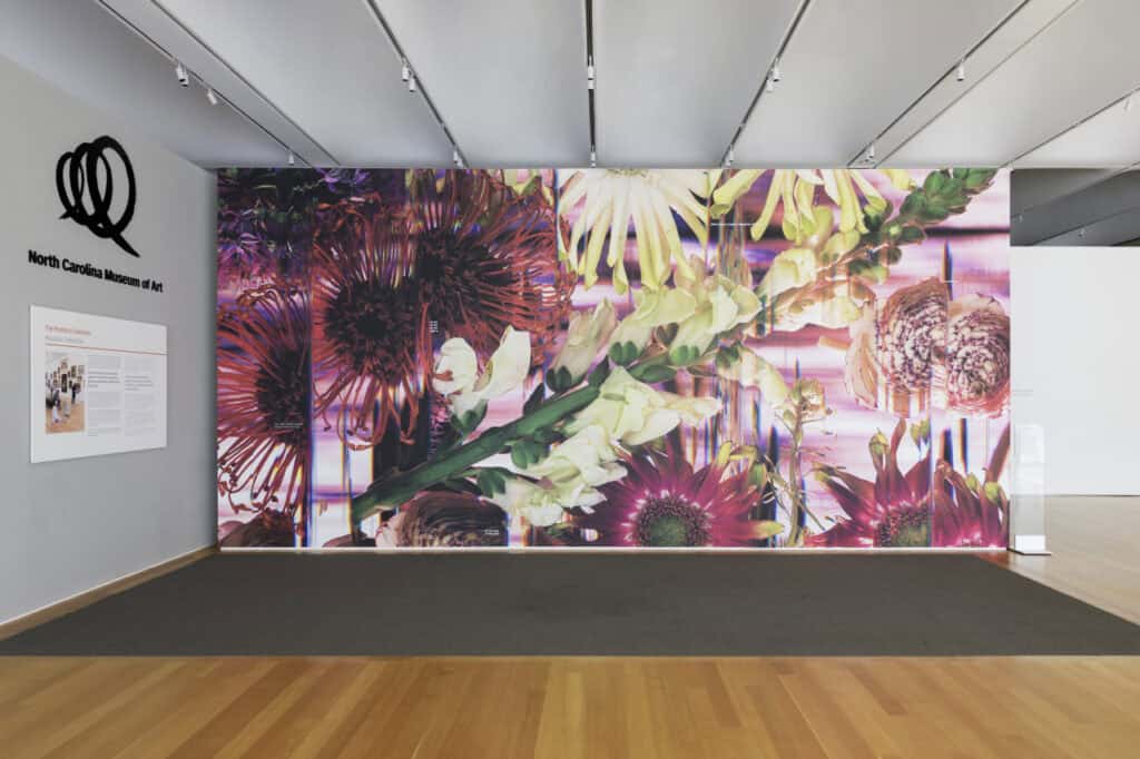 Mural of large-scale digital images of vibrant flowers covering a wall in an art gallery.