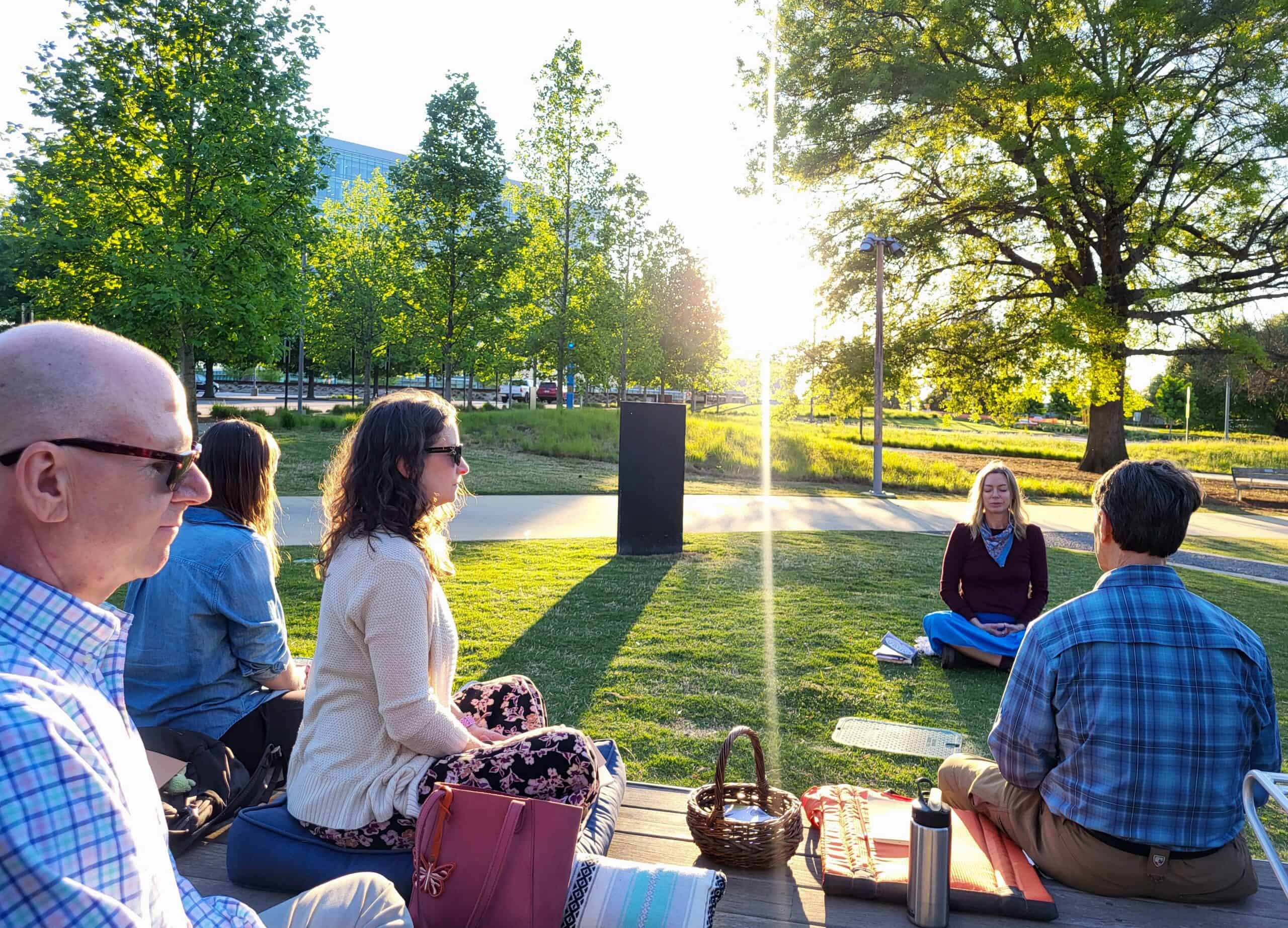 People sit outside in meditative positions with their eyes closed as the sun sets behind them.