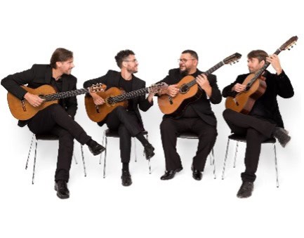 Four men holding guitars sit on chairs and look at each other.