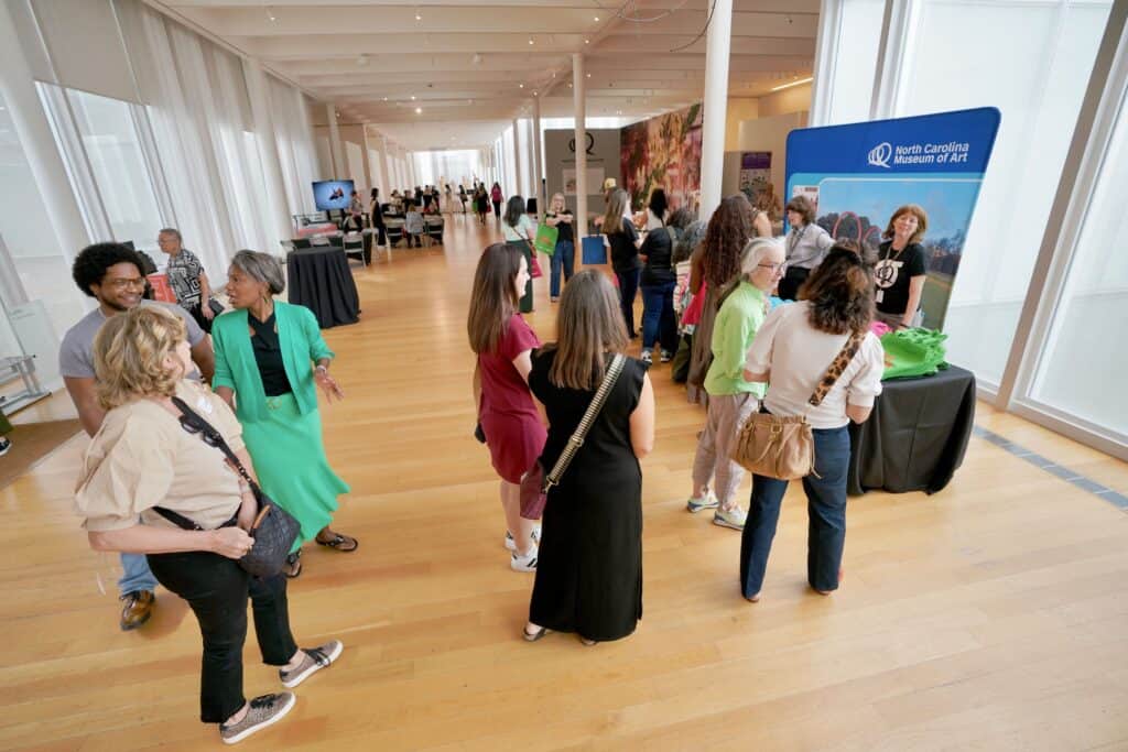 People greet each other as they enter an event in a long lobby-like space.
