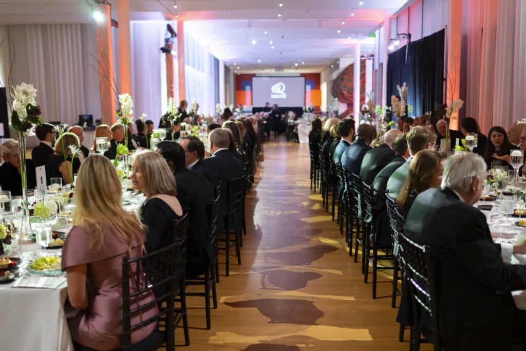 A group of people sitting at the long tables and having dinner.