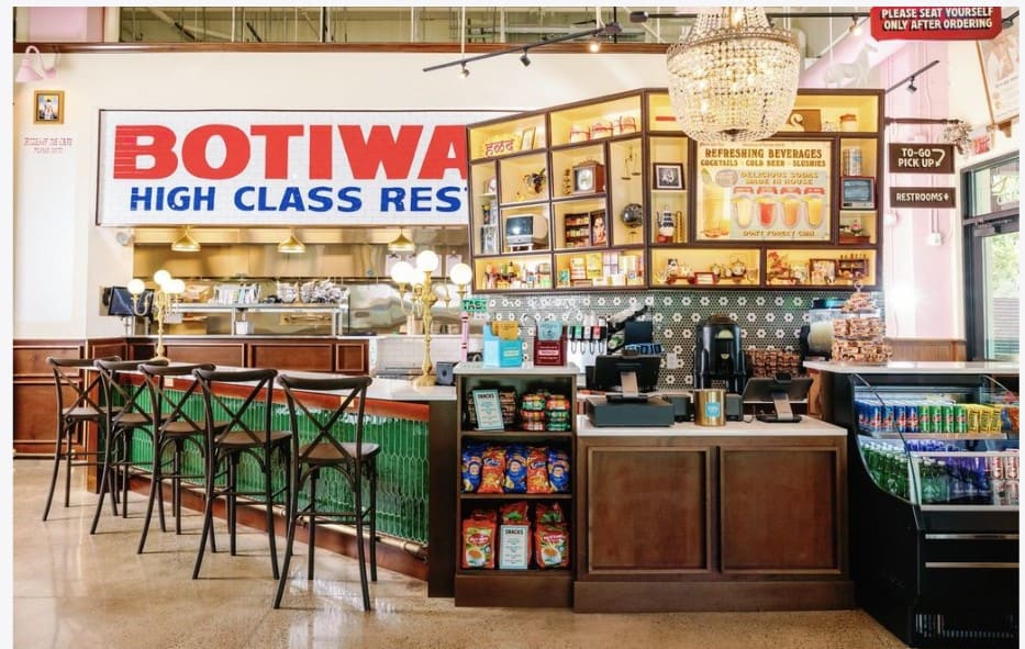 Interior of a restaurant that features a counter with high chairs, countertop terminals, and drink cooler.