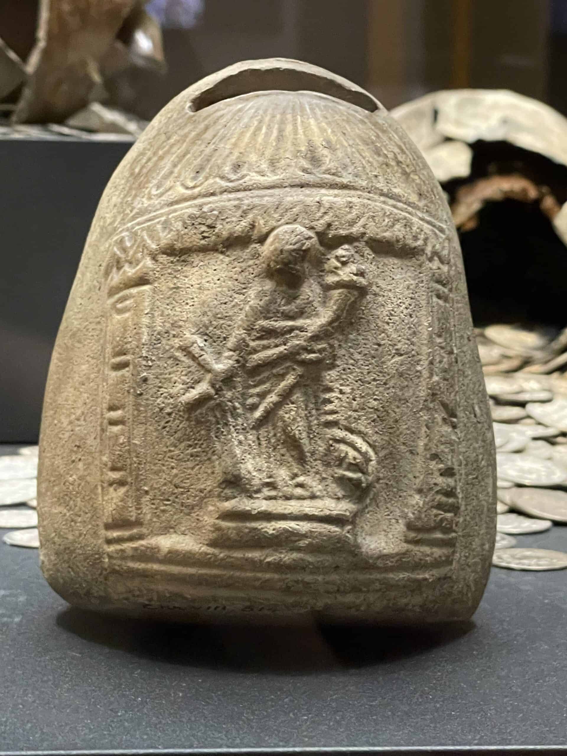 Ceramic jar with a low relief of a figure on the front and a slot at the top.