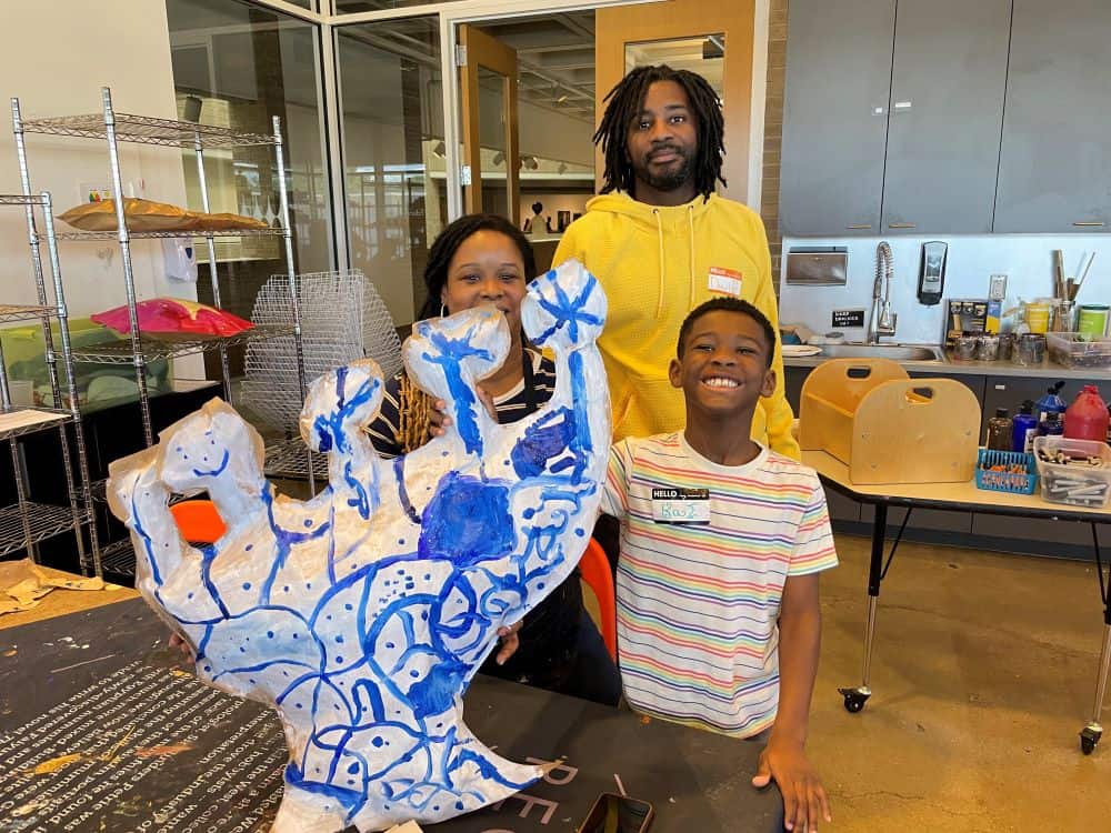 A family poses behind a large white and blue sculpture in an art studio.