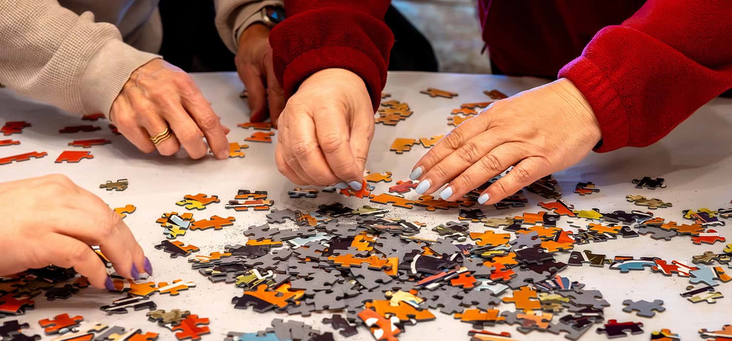 Hands work at flipping jigsaw puzzle pieces over on a table.