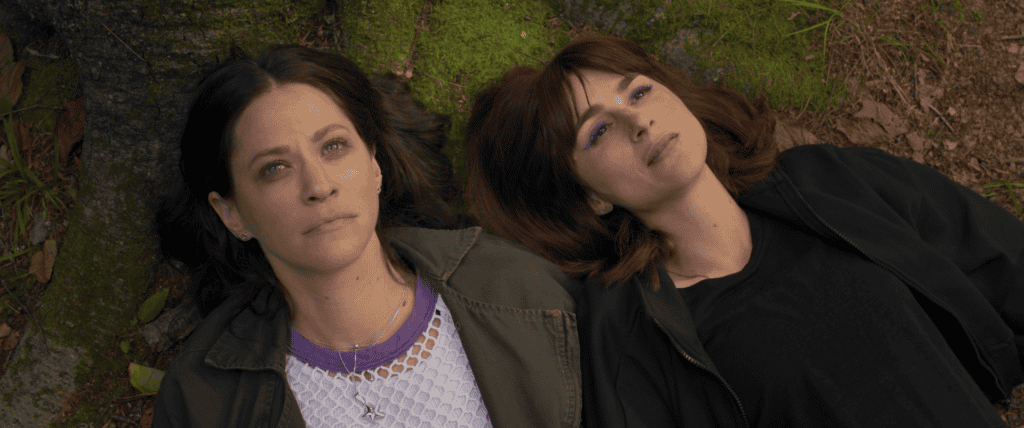 A close-up of two women lying next to each other on grass and looking up.