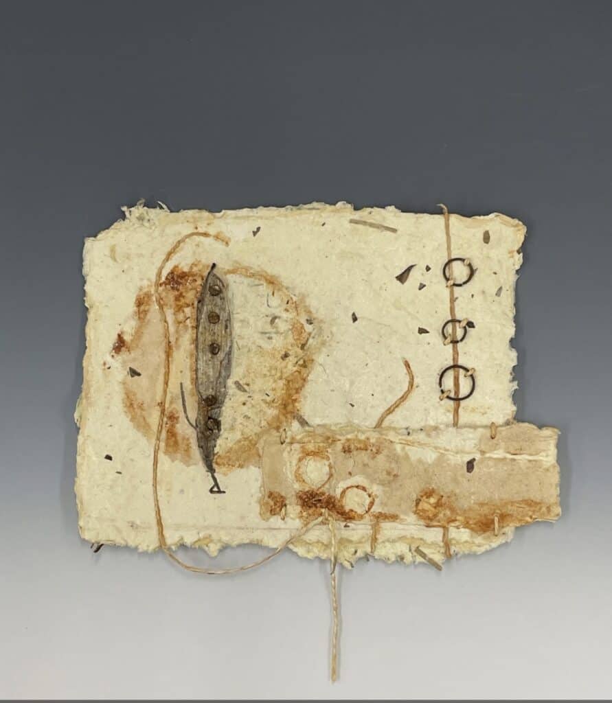 Sheet of handmade paper with deckled edges and inclusions such as metal rings and string.