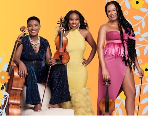 Three women in colorful evening attire hold stringed instruments, look out at the viewer, and smile.