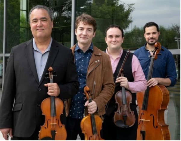 Four men standing in a line diagonal to the picture plan hold stringed instruments, look out at the viewer, and smile.