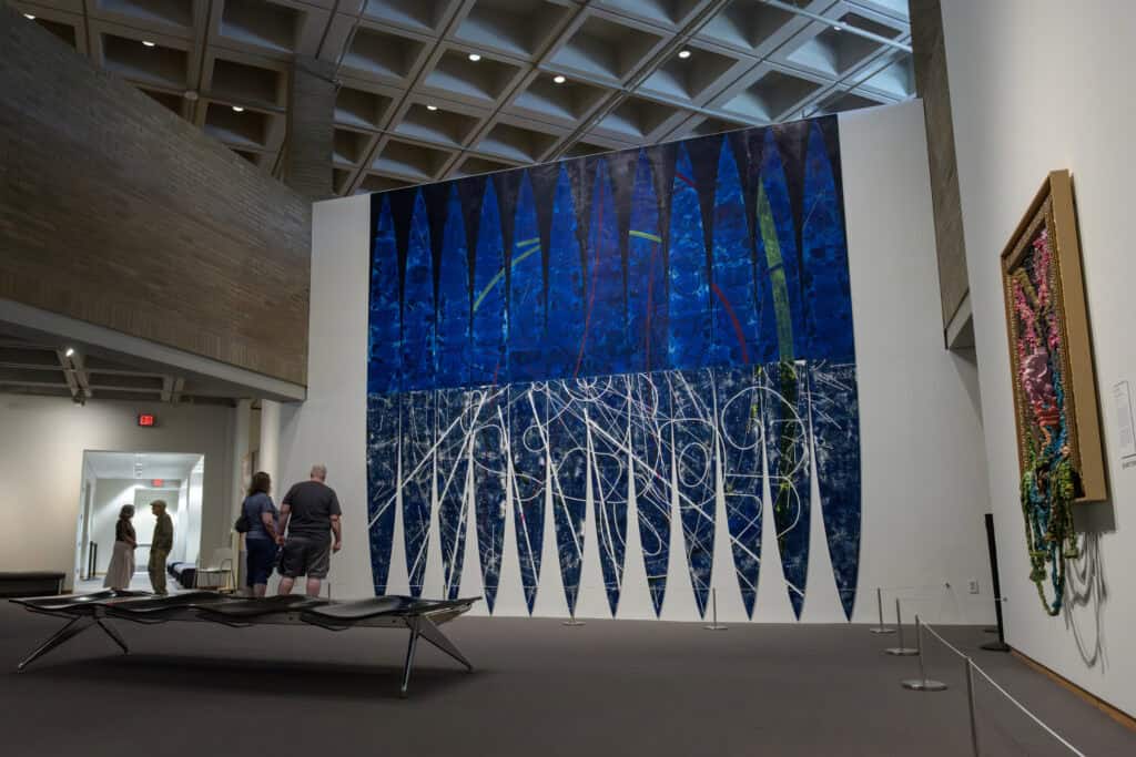 A blue wall mural with a man and a woman standing in front of it to view.