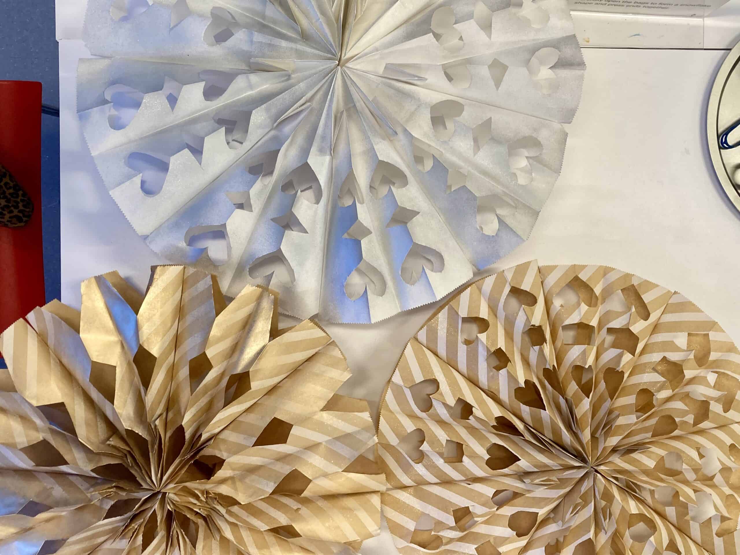 Three large, intricately cut snowflakes made with white and striped brown paper.