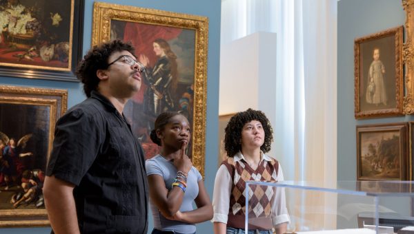 image of college students in the galleries talking together and looking at artwork. Models are NCMA interns Elizabeth Wilson, Luis Roman, and Imani Cosby.